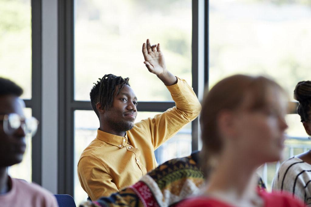 A student raises his hand in a lecture hall