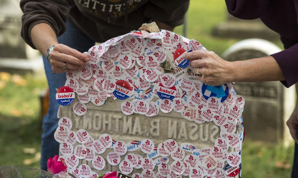 Hands place "I voted today" stickers on Susan B. 安东尼的墓碑.