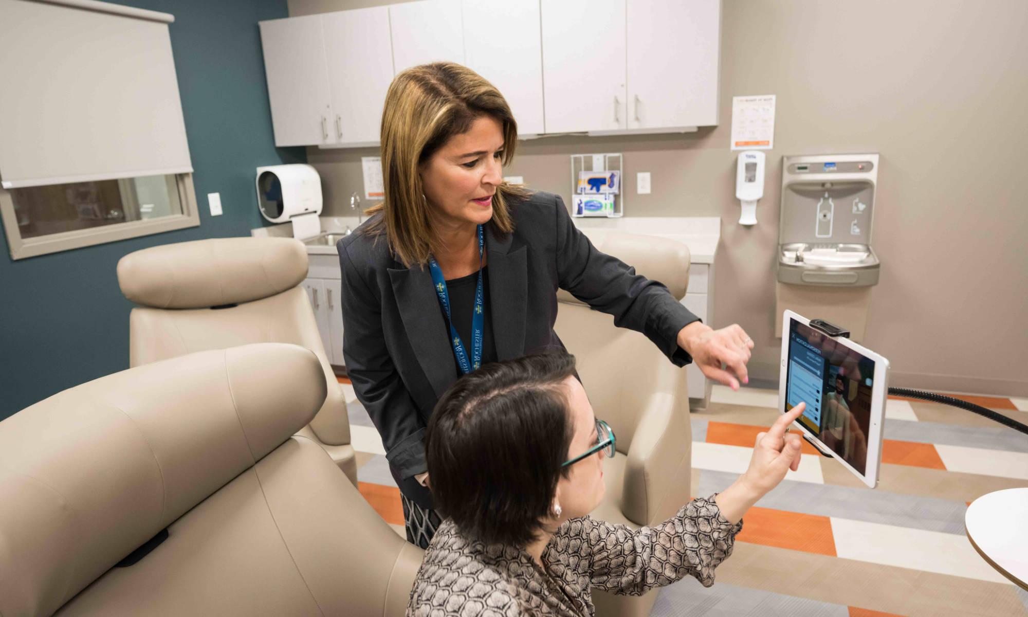 Two clinicians in a hospital-like setting touch the screen of a mounted tablet.